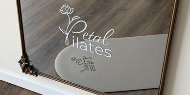 A Pilates studio with a mat and mirror showing the Petal Pilates logo.