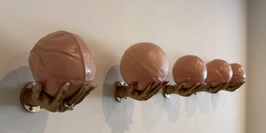 Sculptural hands holding spheres mounted on a wall in descending size order.
