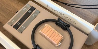 Pilates reformer with resistance bands and a Pilates ring on a wooden floor.