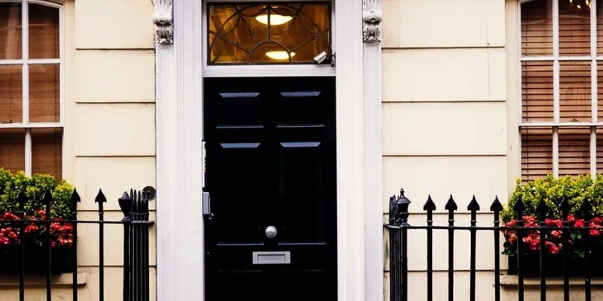 Elegant black door framed by white pillars and iron fence with flowers.