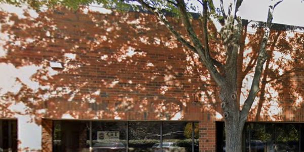 Brick building facade with large windows and a tree casting shadows.