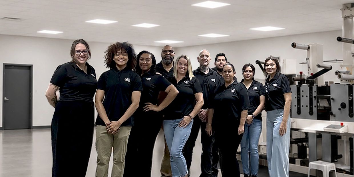 A group of ten employees in black shirts posing in a clean industrial workspace.