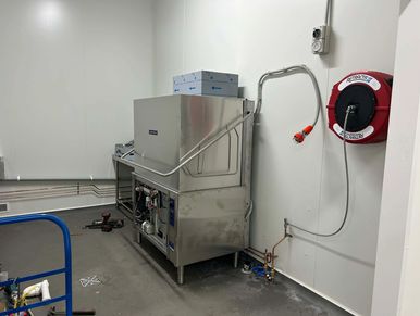 Industrial dishwasher in a clean utility room with tools and hose reel.