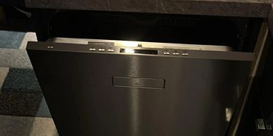 Stainless steel dishwasher with a rubber mat in front on a wooden floor.