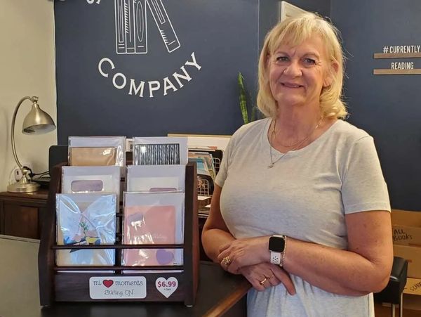 A woman stands smiling next to a card display in a cozy shop.