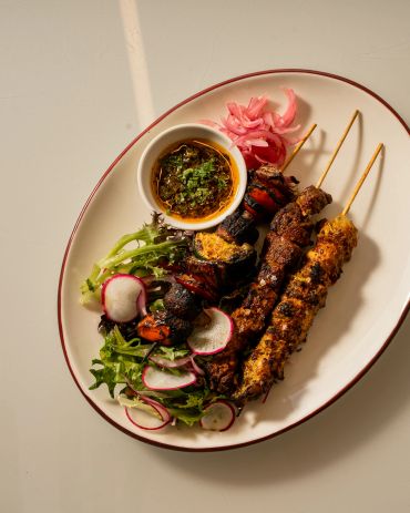 Plate with grilled skewers, salad, and dipping sauce.