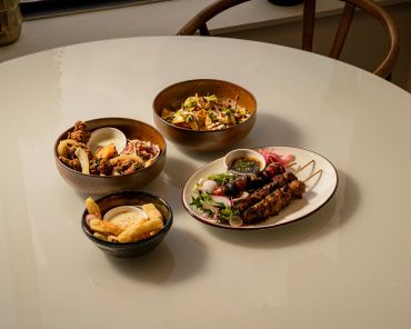 Four bowls and plates with various dishes on a table.