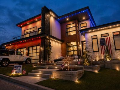 Modern house decorated with 4th of July lights and flags at night.