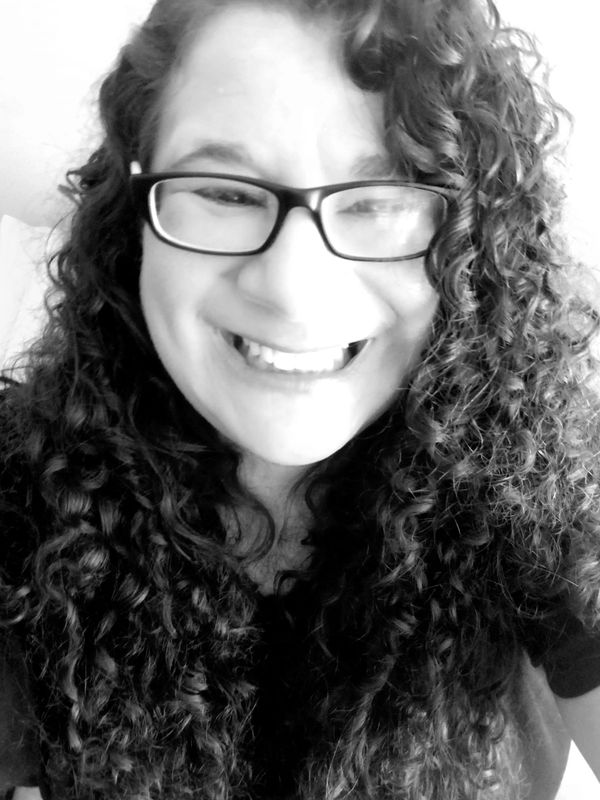 Black and white close-up of a smiling woman with curly hair and glasses.