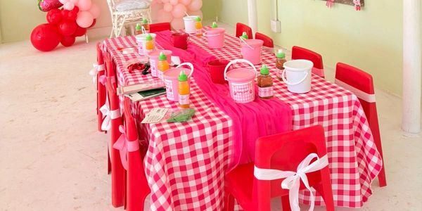 Kids Party, strawberry theme with Red and white checkered table set with craft supplies and decorated chairs.