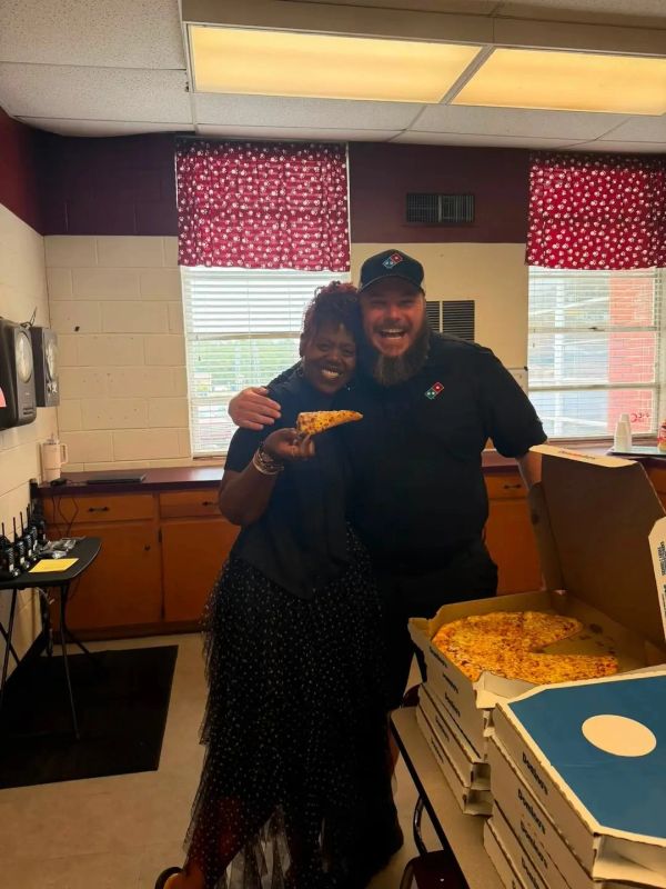Two smiling people with Domino's pizza in a kitchen.