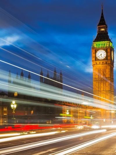 Big Ben illuminated at night with light trails from passing vehicles.