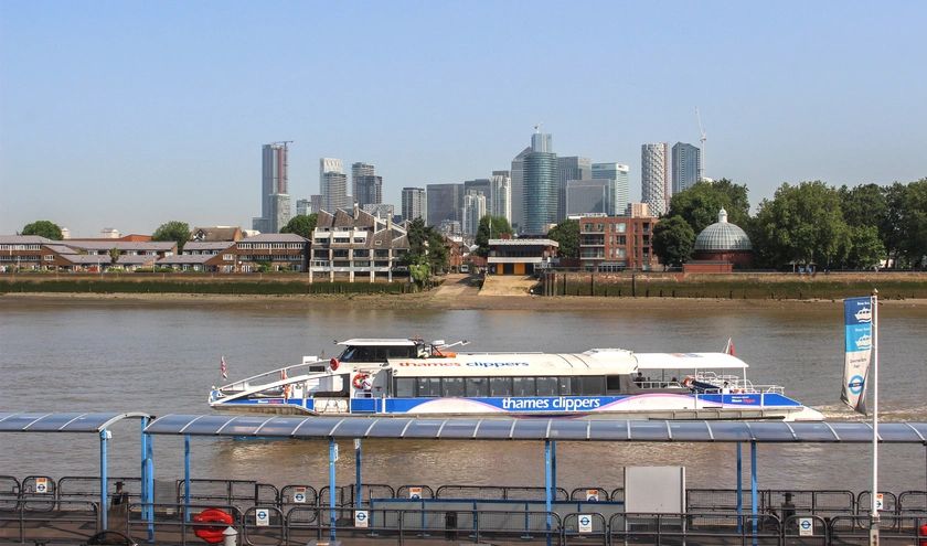 Thames Clippers boat cruising on the river with city skyline in the background.