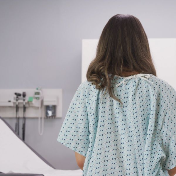 Woman in hospital gown facing away in a medical room.