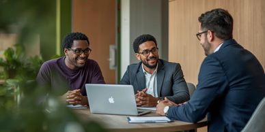 Three men having a friendly business meeting at a table with a laptop.