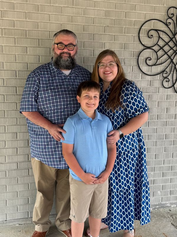 Smiling family of three posing in front of a brick wall.