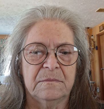 Elderly woman wearing glasses with a neutral expression indoors.