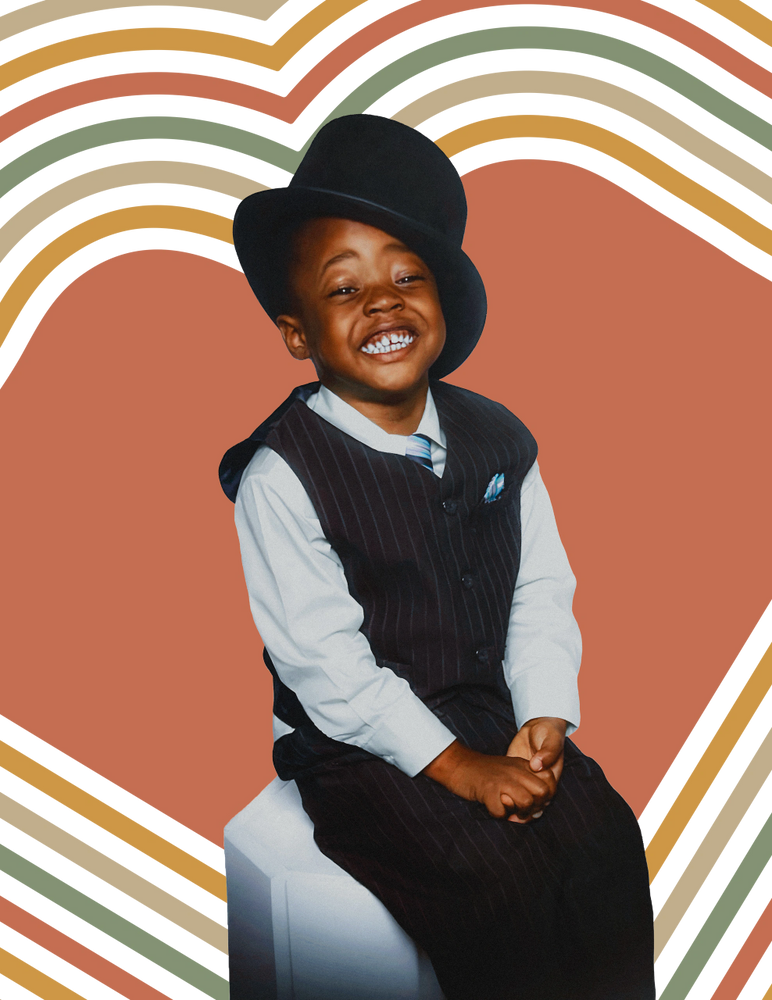 Smiling child in a pinstripe suit and top hat, sitting against a colorful heart-patterned background.