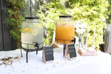 Two beverage dispensers with lemon water and peach iced tea on a decorated table.