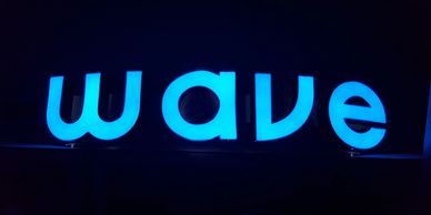 Glowing blue neon sign spelling 'wave' on a dark background.