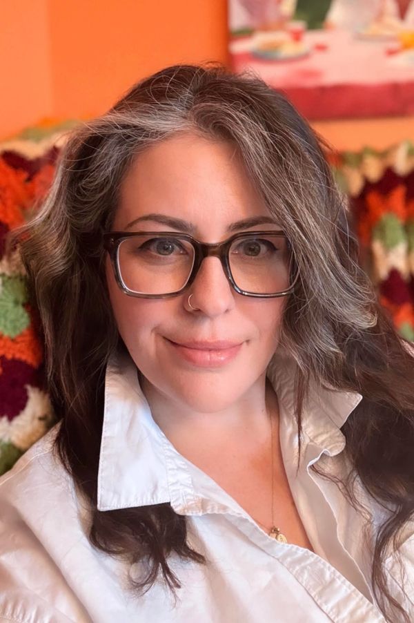 Woman with glasses and a white shirt smiling indoors.