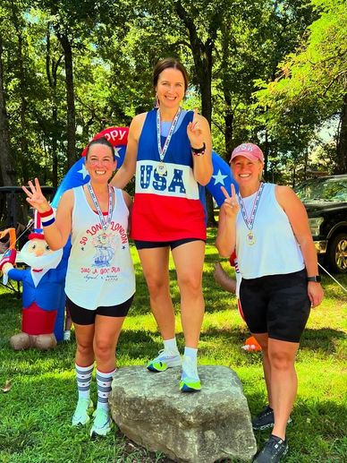 Three women celebrating on a podium outdoors with medals.