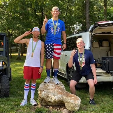 Three men celebrating victory outdoors, wearing medals.