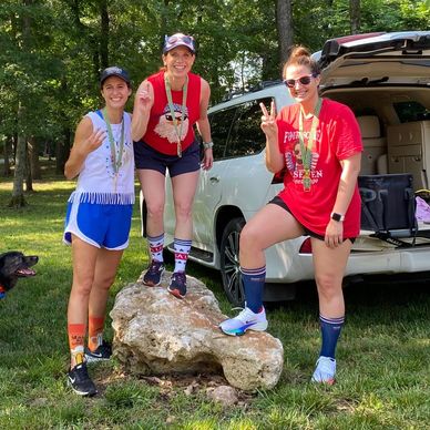 Three women posing outdoors with medals, making peace signs.