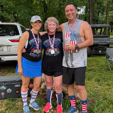 Three people with medals pose outdoors after a race.