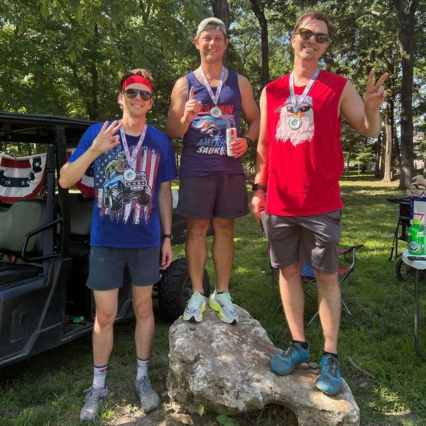 Three men with medals posing outdoors after a race.