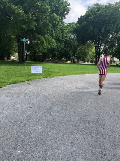 Person in patriotic attire walking on a street near a grass patch with a sign.