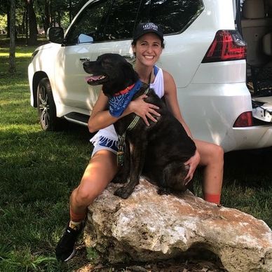 Woman happily hugging a black dog outdoors beside a white SUV.