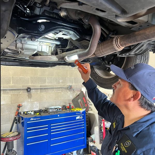 Mechanic inspecting the underside of a car with a flashlight in a workshop.