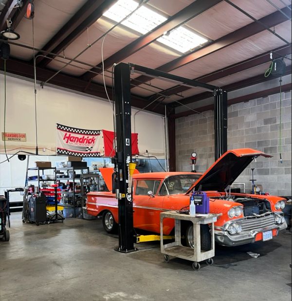 Classic orange car being serviced in a spacious garage with Hendrick Motorsports banner.
