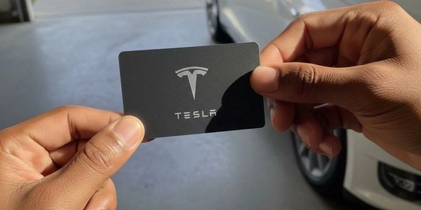 Hands holding a black Tesla card with a car in the background.