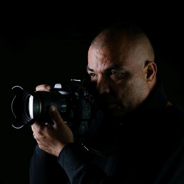A man intensely focusing through a Nikon camera in low light.