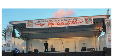 wide view of covered mobile stage with large “Pop-Up Talent Show” banner and side branding