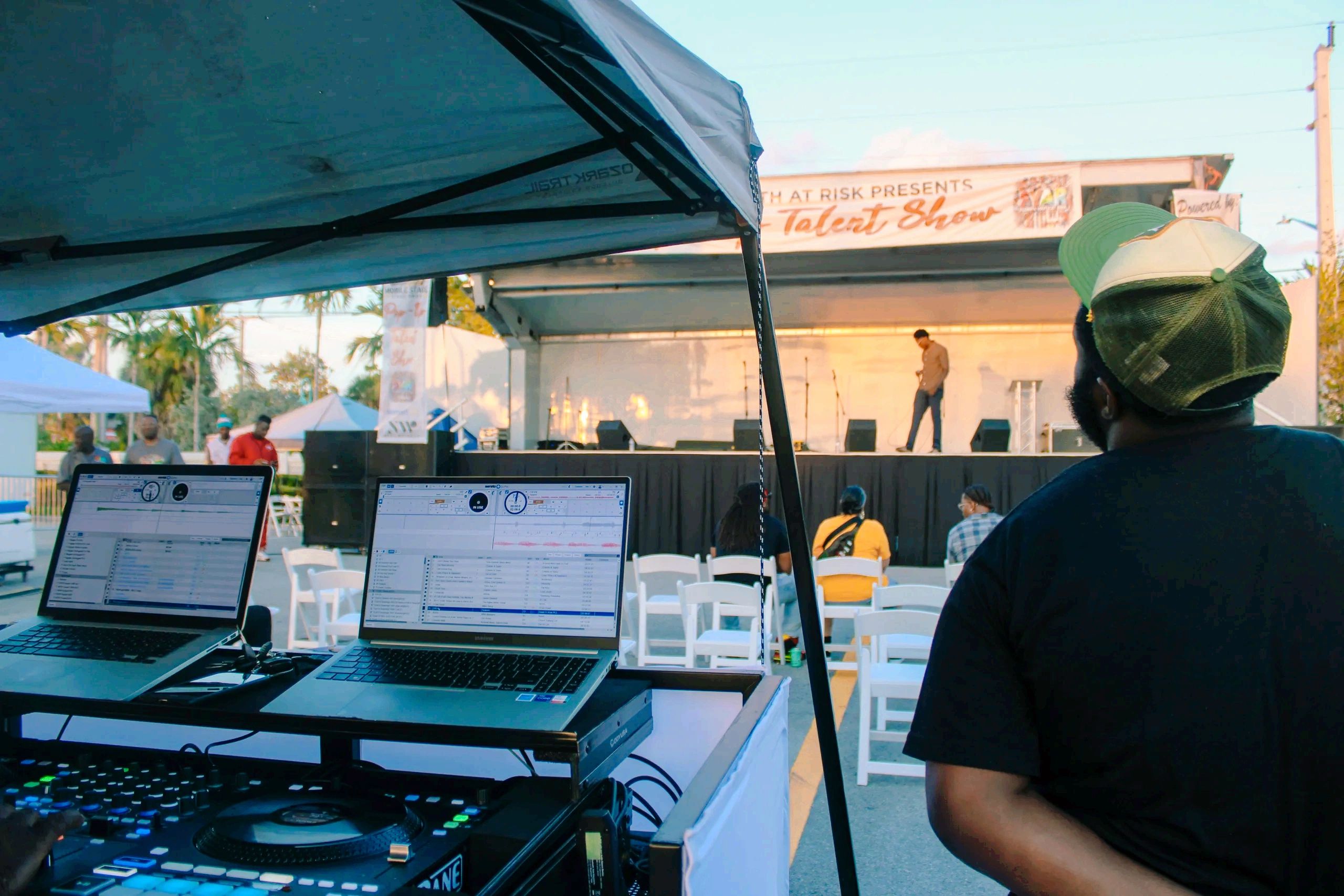 DJ  with laptops and mixer facing Mobile Stage Pros covered stage at a South Florida outdoor event