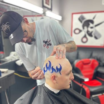 Barber creating a blue flame design on a shaved head.