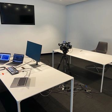 A room with blank walls, with a chair set up in front of a video camera and a computer set up for ed