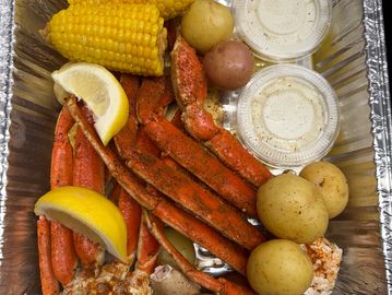 Crab legs with potatoes, corn, and lemon wedges.