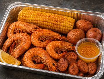 Seafood boil with shrimp, corn, potatoes, and dipping sauce.