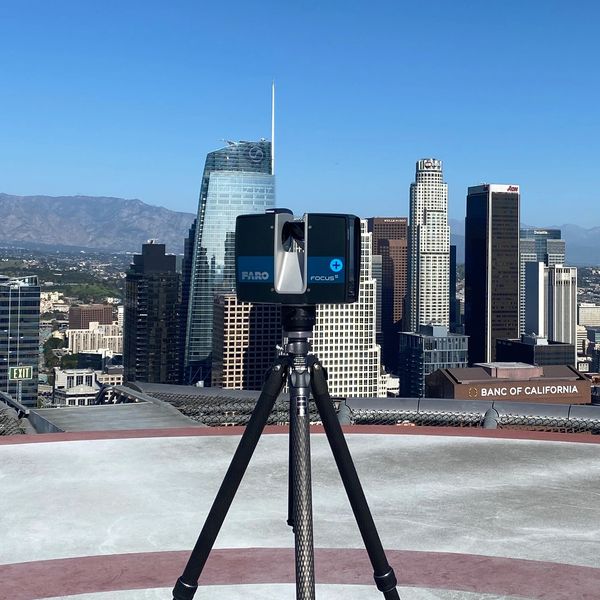 A laser scanner on a tripod overlooking a city skyline under clear blue skies.