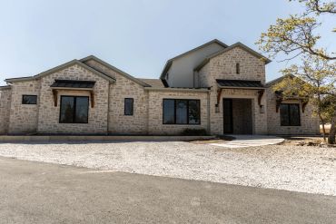 Modern stone house with large windows and gravel driveway.