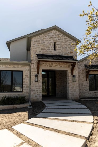Modern stone house with a curved concrete pathway leading to the entrance.