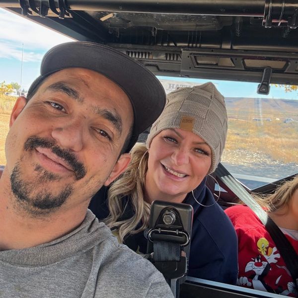 Two people smiling inside a vehicle on a sunny day.