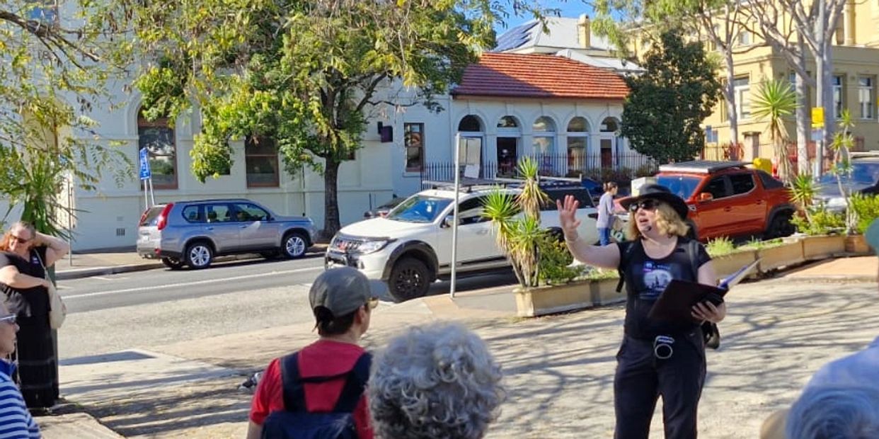A woman in black leads a group outdoors on a sunny day.