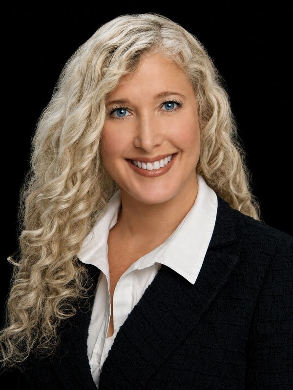 Smiling woman with blonde curly hair in professional attire.