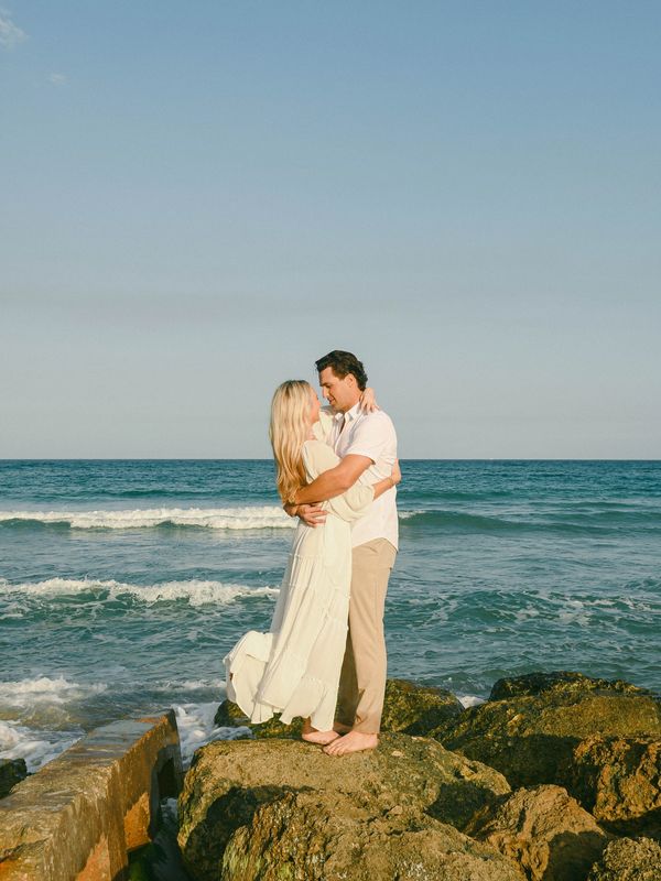 Couple embracing on rocks by the ocean.