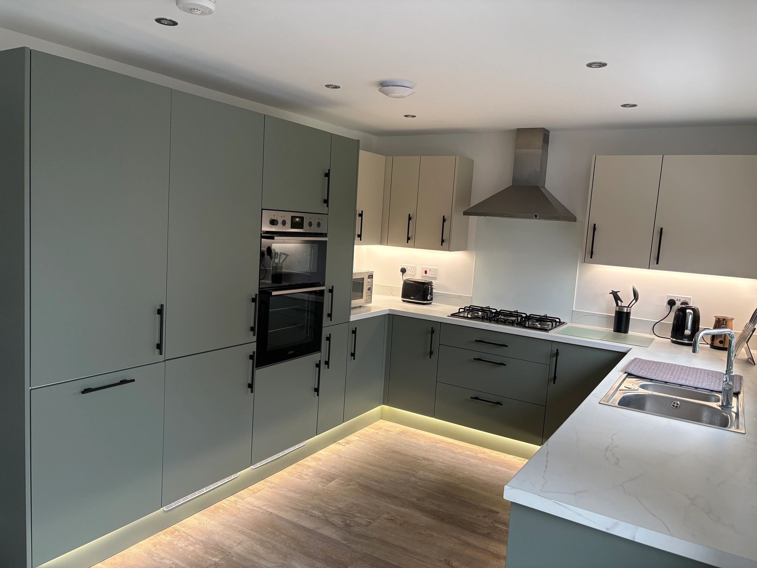 Modern kitchen with green and beige cabinets and under-cabinet lighting.